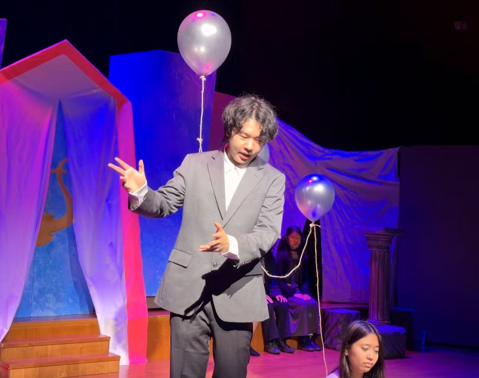 Guoshwan on stage as Eurydice’s Father, holding a balloon in the SHSID Drama Club production